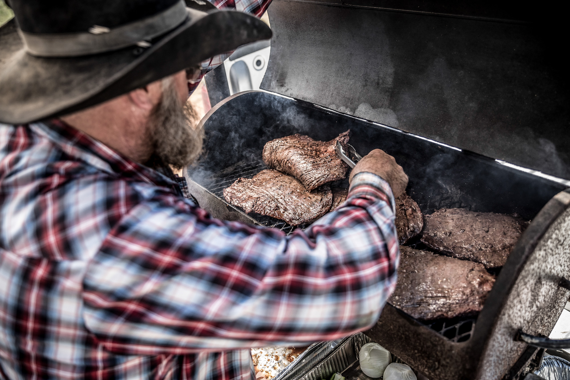 cowboy grilling flank steaks on outdoor gill