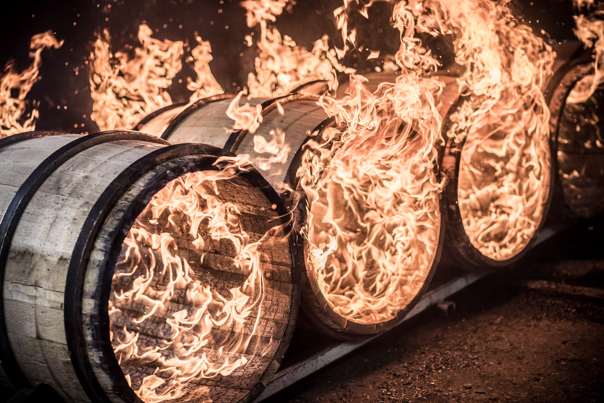 4 wooden whiskey barrels on fire flame being charred for whiskey at independent stave company in kentucky