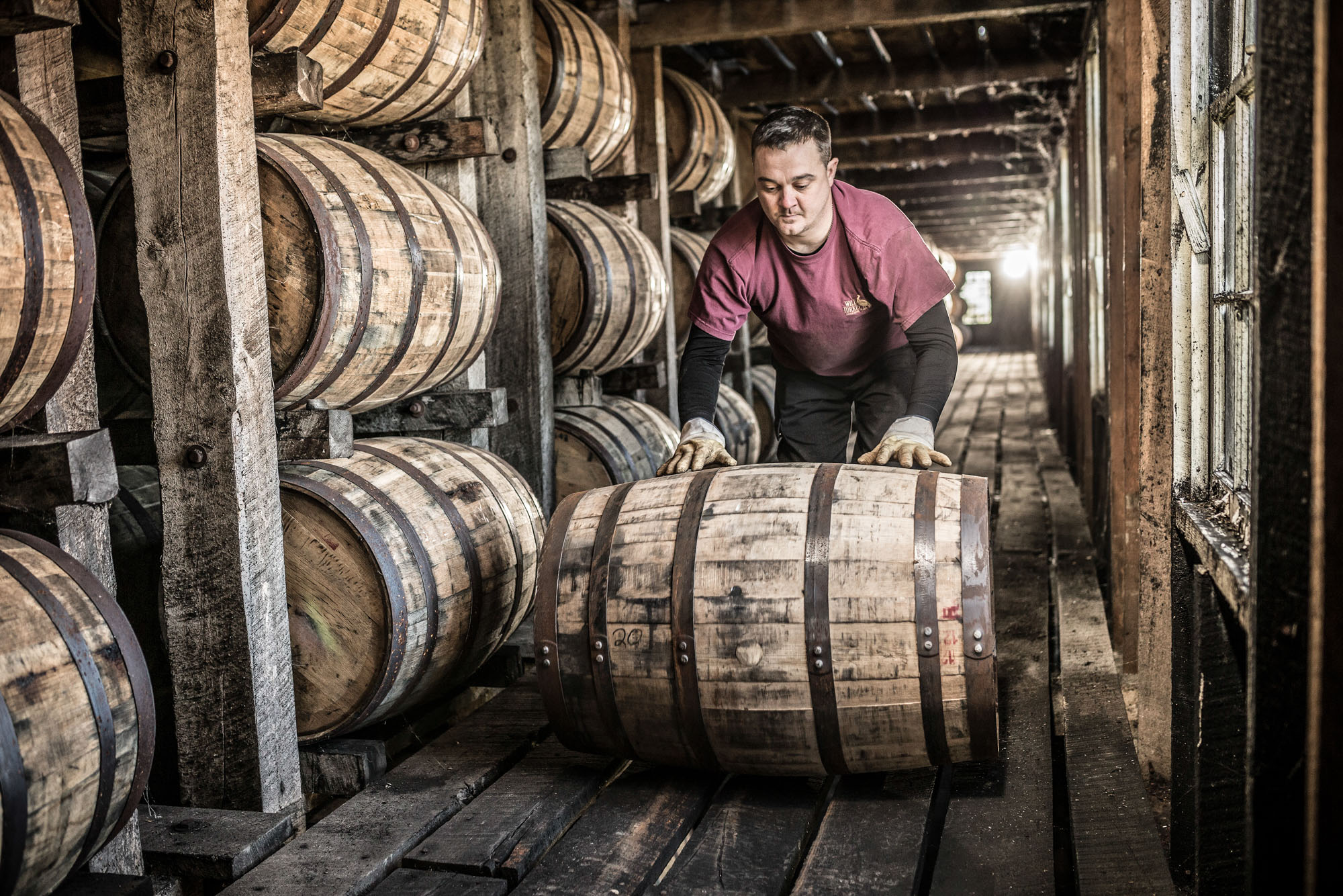 man rolling whiskey barrel in rick house at wild turkey russells reserve bourbon whiskey barrel storage building house in kentucky