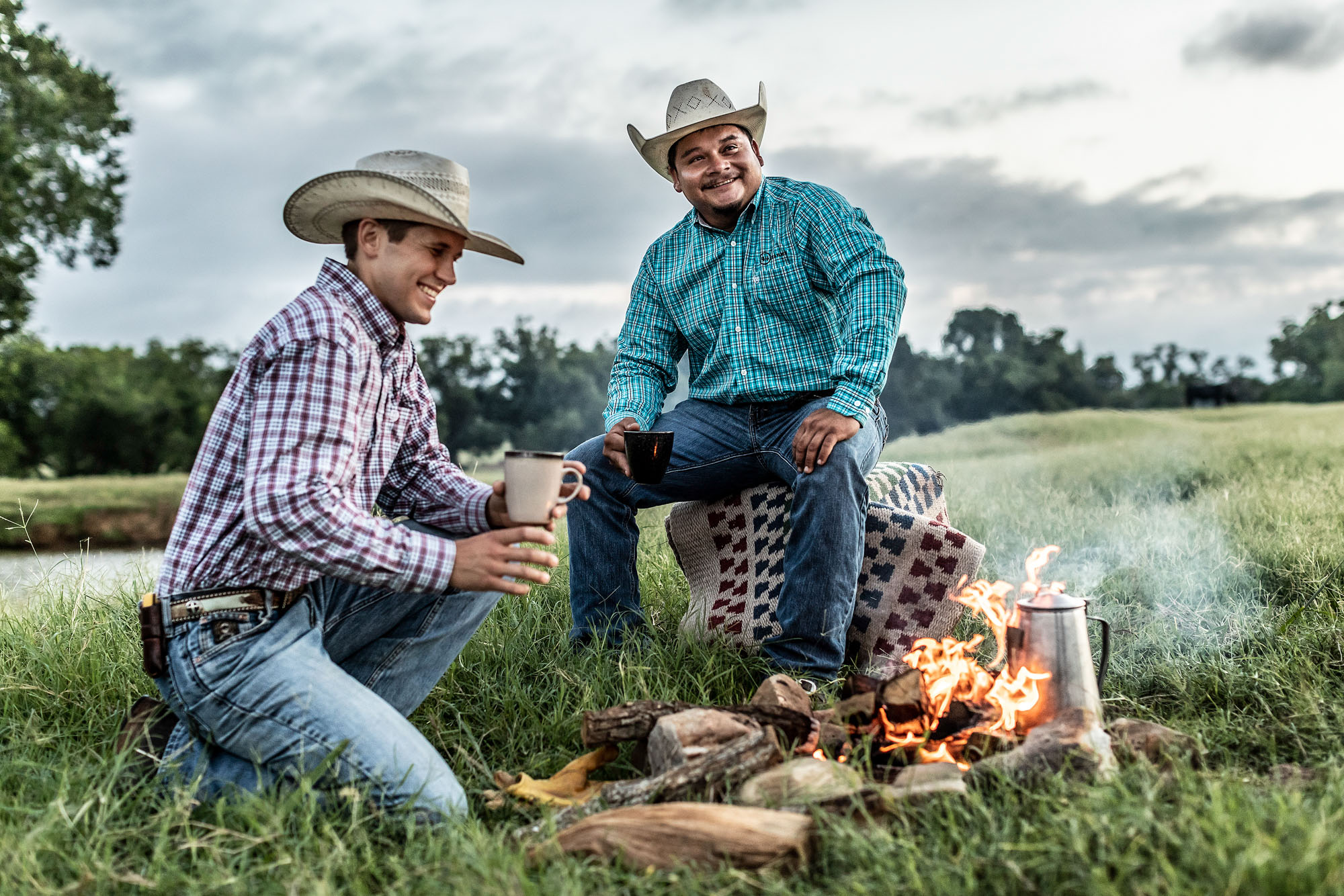 cowboys sitting by fire drinking coffee in field at sunrise sunset