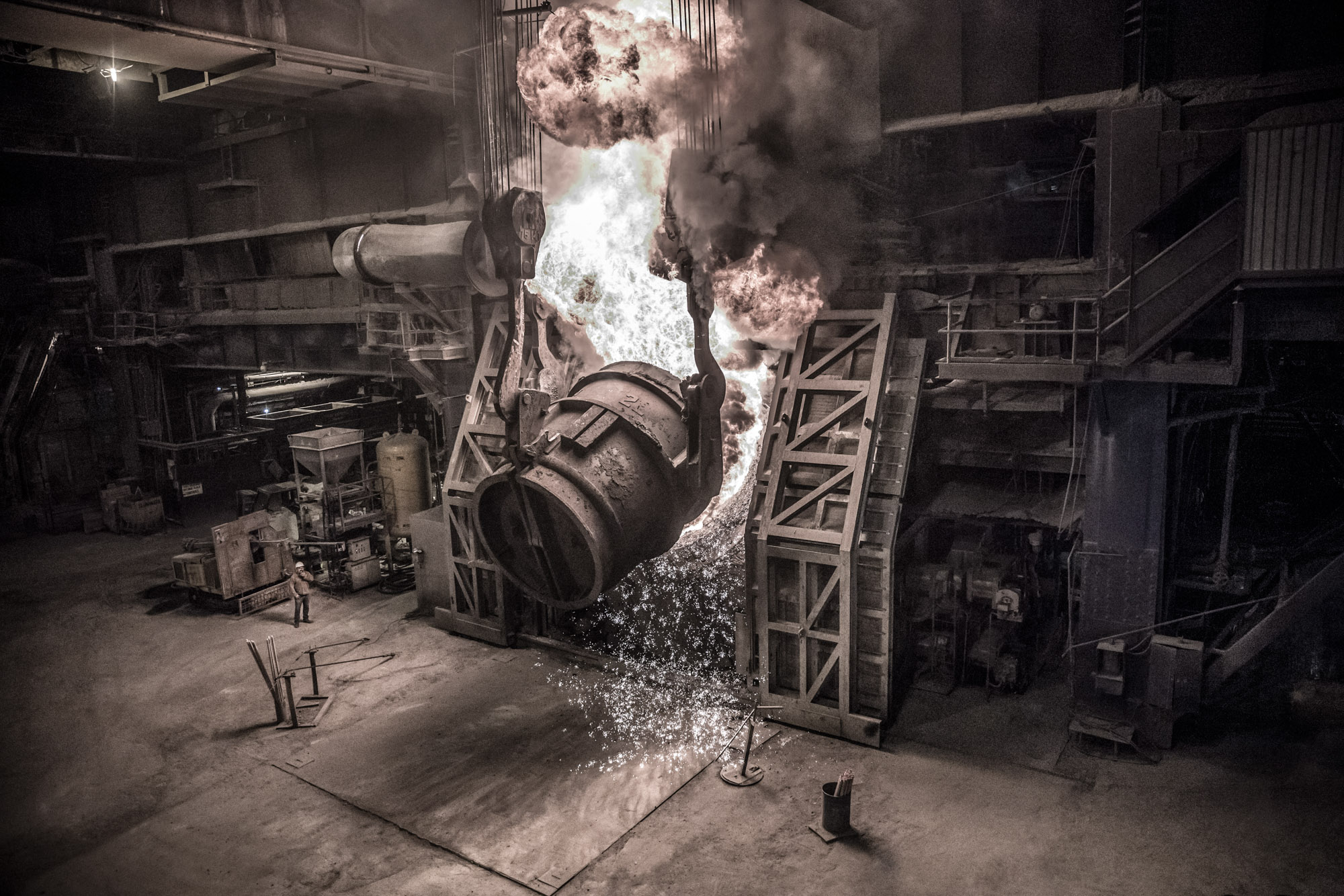 large container of molten steel being poured in to with sparks and fire coming up out