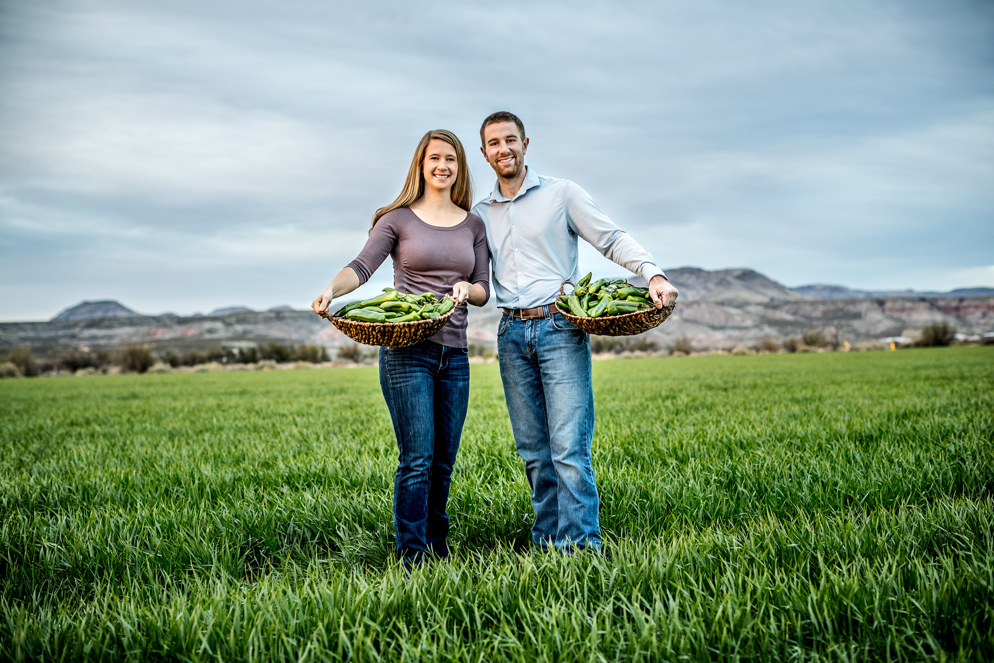portrait of the owners of hatch chili company holding chilis and standing in green field