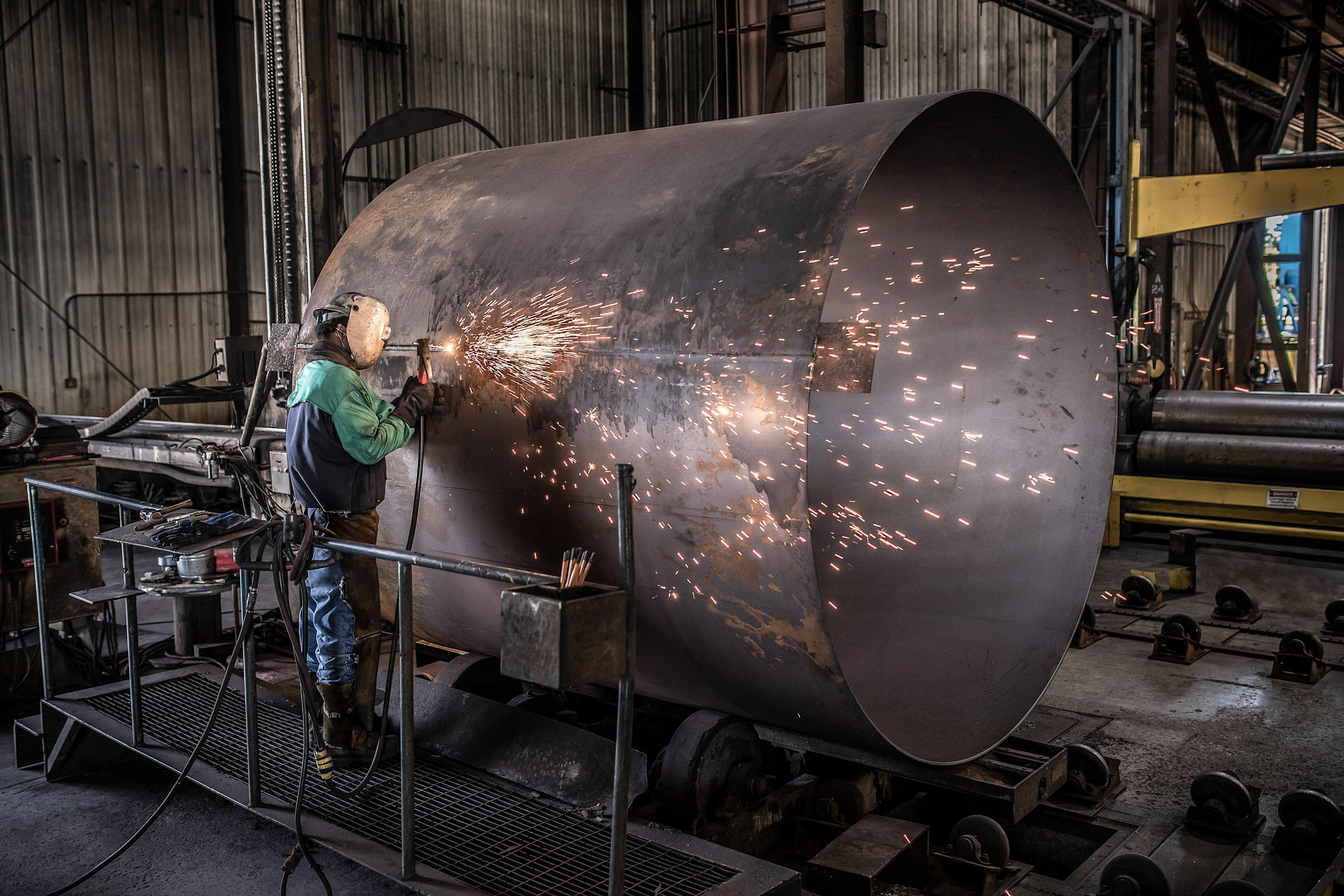man welder welding tank in industrial plant with sparks