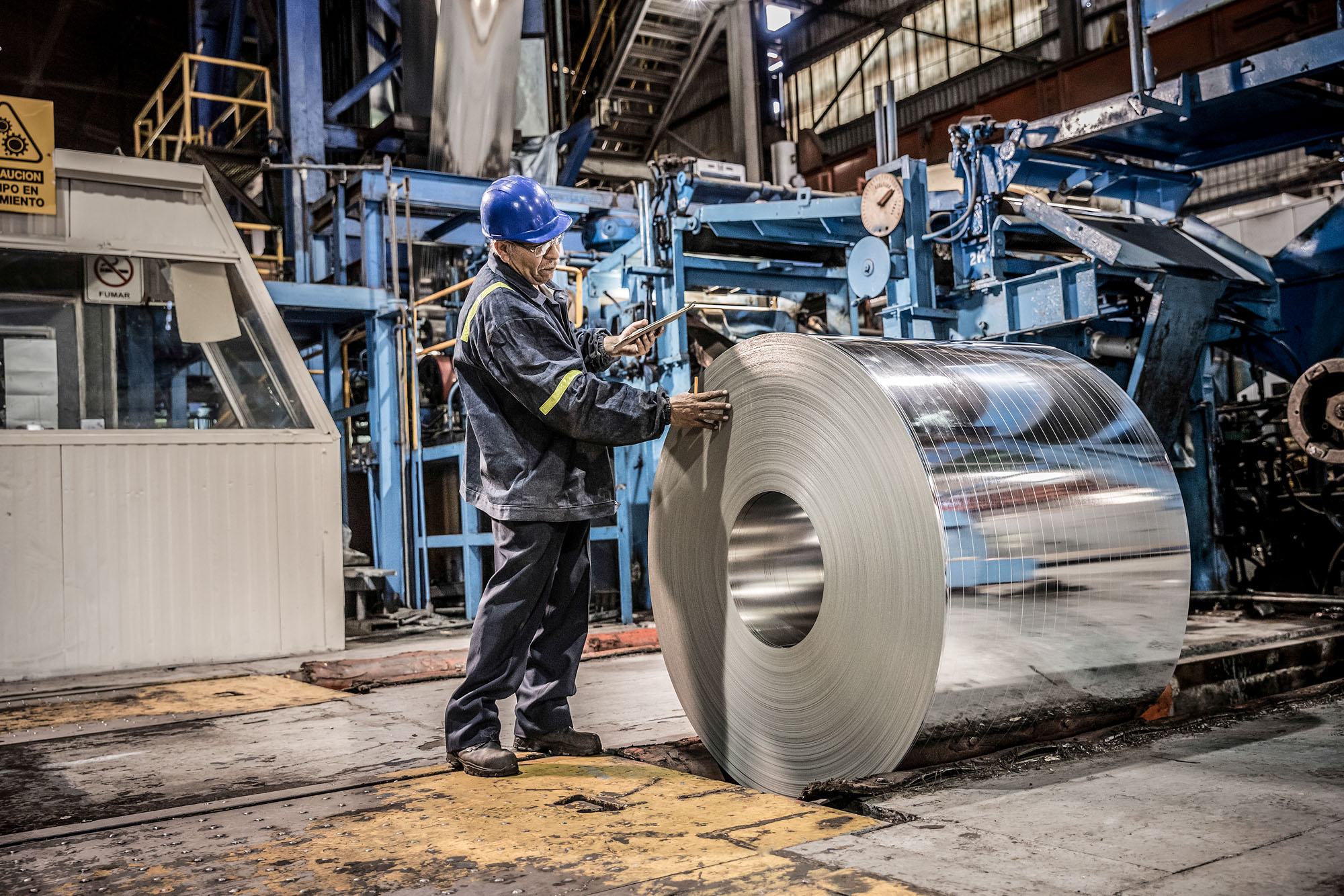steel worker man inspecting large roll of thin sheet steel at steel mill